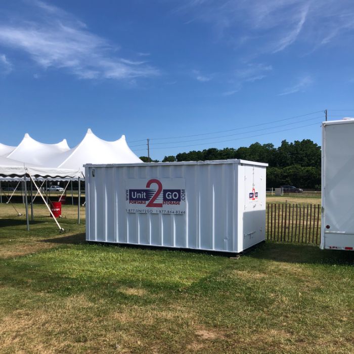 a Unit2Go portable storage unit next to an outdoor event tent under a blue sky